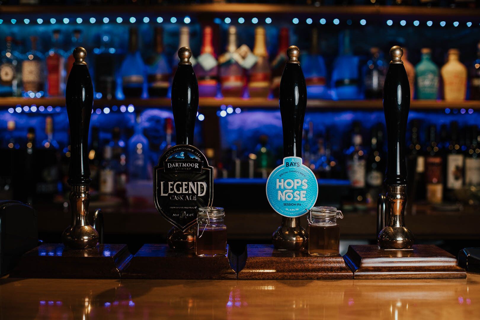 Un bar con cuatro grifos, incluyendo 'Legend Cask Ale' y 'Hops Nose Session IPA'.
