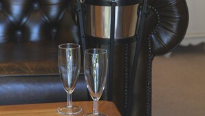 A champagne bottle in a metal bucket on a table with two glasses beside it, in a room with a tufted leather sofa and a bed in the background. - Bearslake Inn (Okehampton)