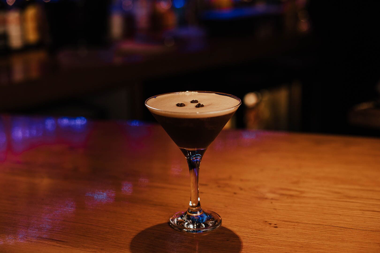 A martini glass with a frothy top on a wooden bar counter.