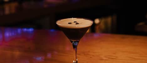 A martini glass with a frothy top on a wooden bar counter.