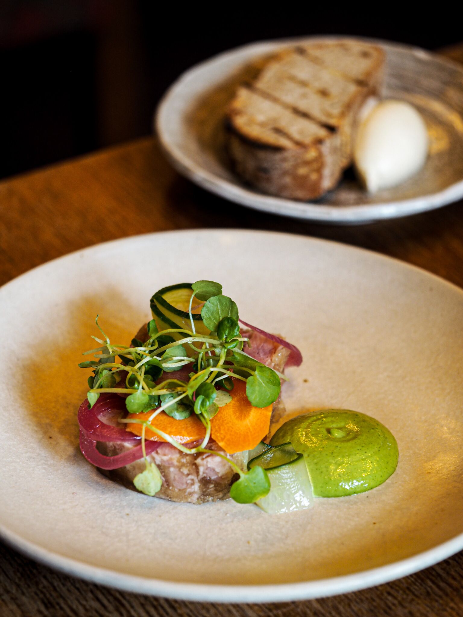 Une assiette de nourriture comprenant une variété de légumes et une tranche de viande, accompagnée d’un morceau de pain et d’un œuf dur, servis sur une assiette à part.