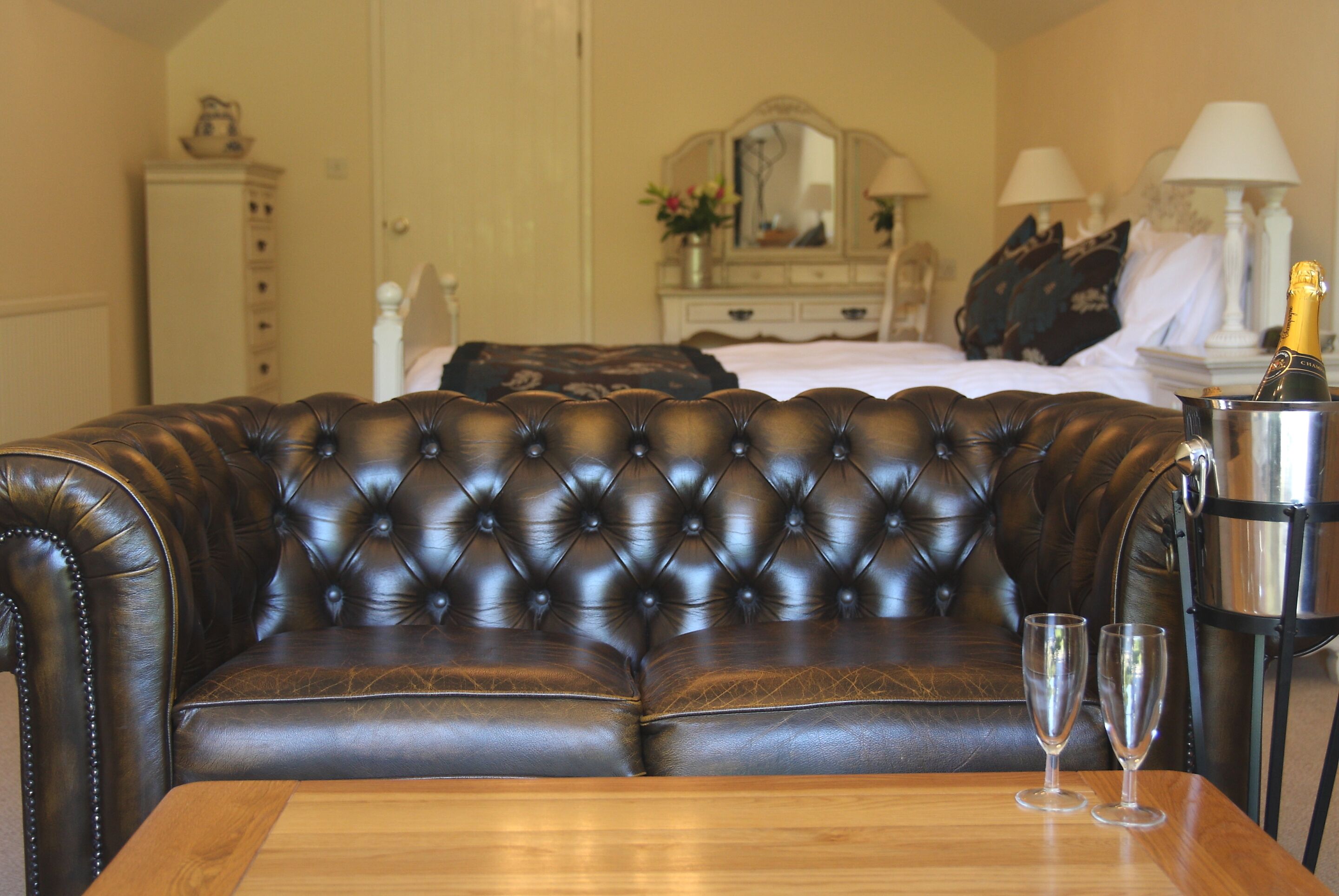 A dark brown leather sofa with a tufted backrest, a wooden table with two clear glasses, and a metal container with a bottle.