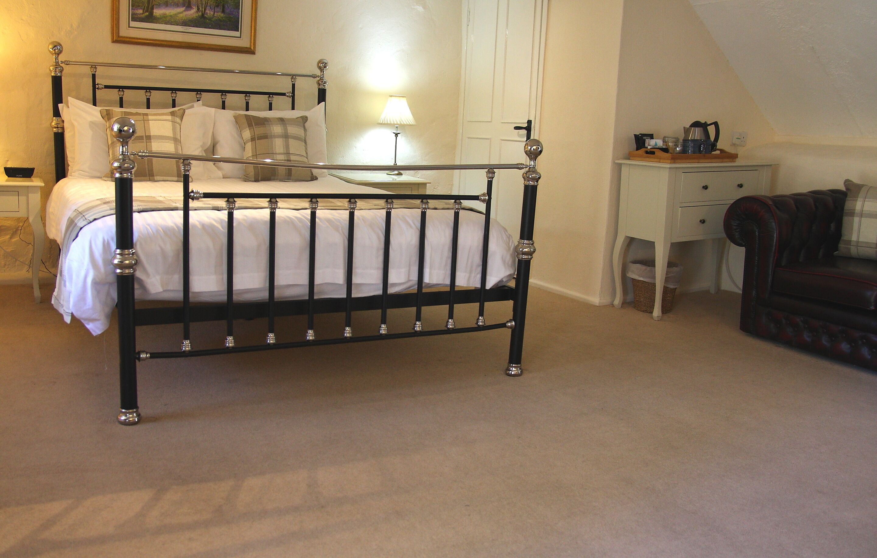A bedroom with a metal-framed bed, a bedside table with a lamp, a desk, and a leather sofa.