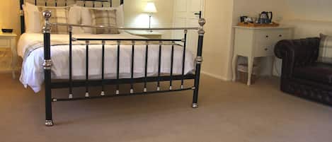 A bedroom with a metal-framed bed, a bedside table with a lamp, a desk, and a leather sofa.