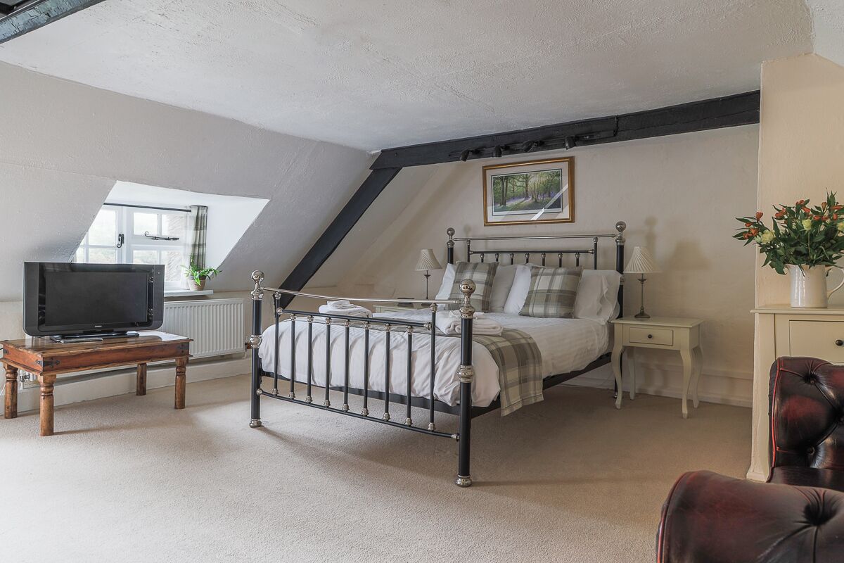 A bedroom with a bed, a television on a wooden table, a nightstand, a lamp, and a chair.