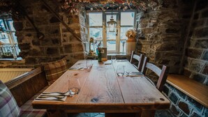 A rustic dining area with a wooden table set for two, stone walls, and a window with a view. - Bearslake Inn (Okehampton)