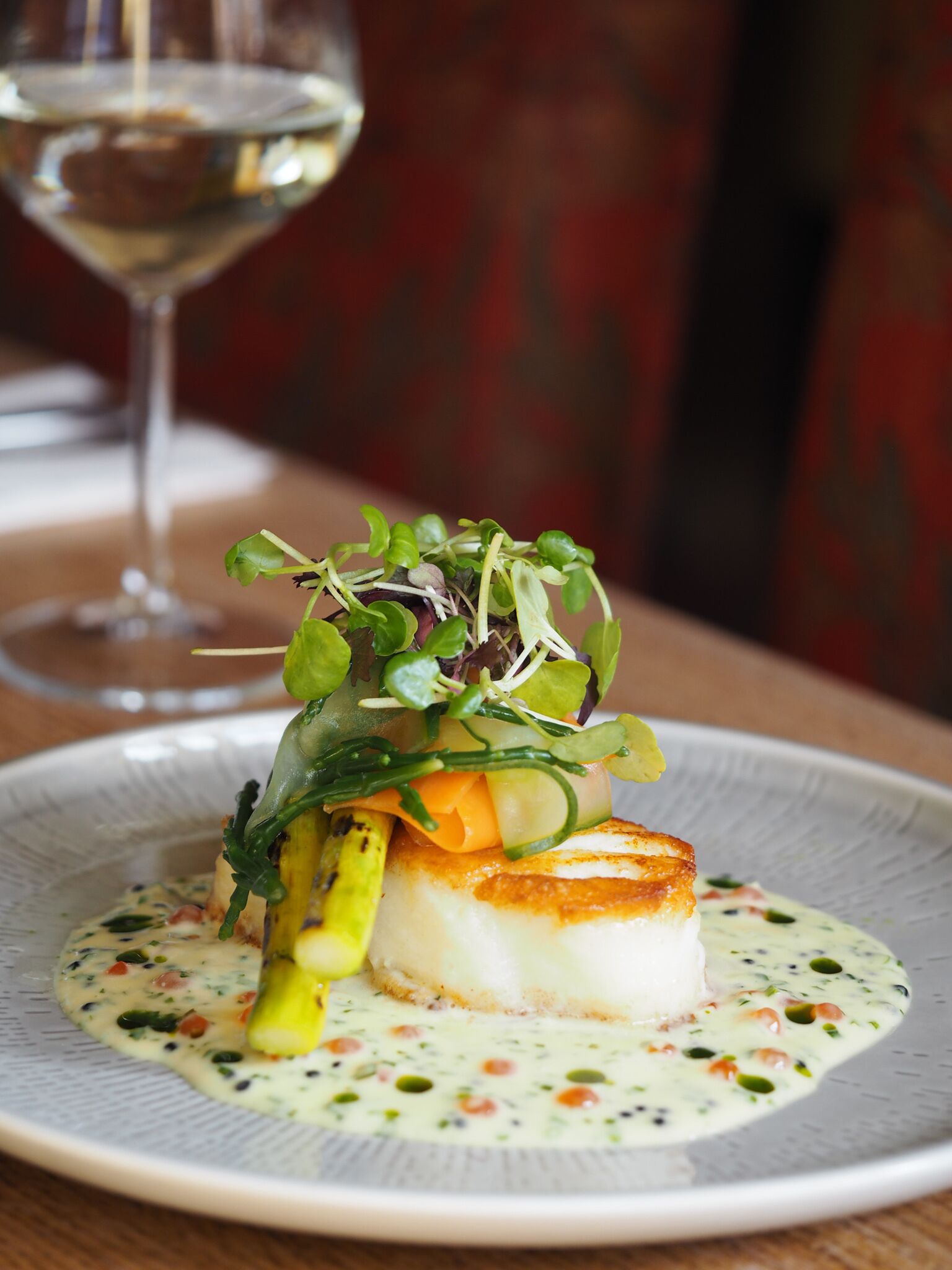 A plate of food with a piece of fish, asparagus, and greens, served on a white plate with a creamy sauce.