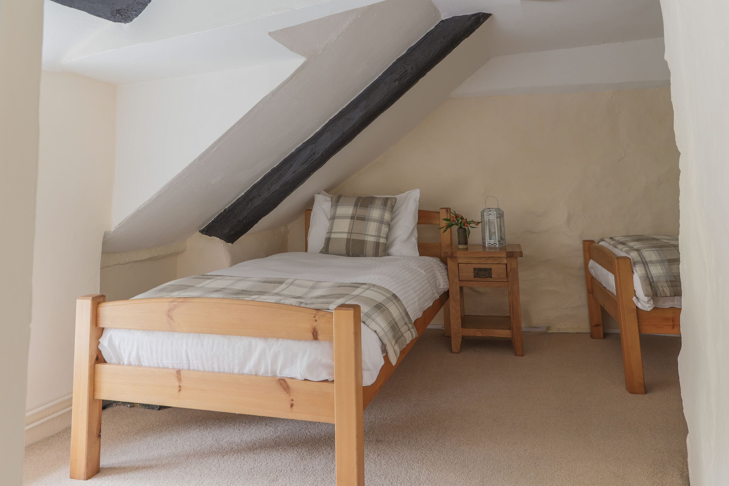 A bedroom with a sloped ceiling, a wooden bed, a bedside table, and a small bedside table with a lamp.