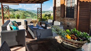 Eine Terrasse im Freien mit Korbmöbeln, einem Tisch mit einer Vase und einem Korb voller Gemüse.
