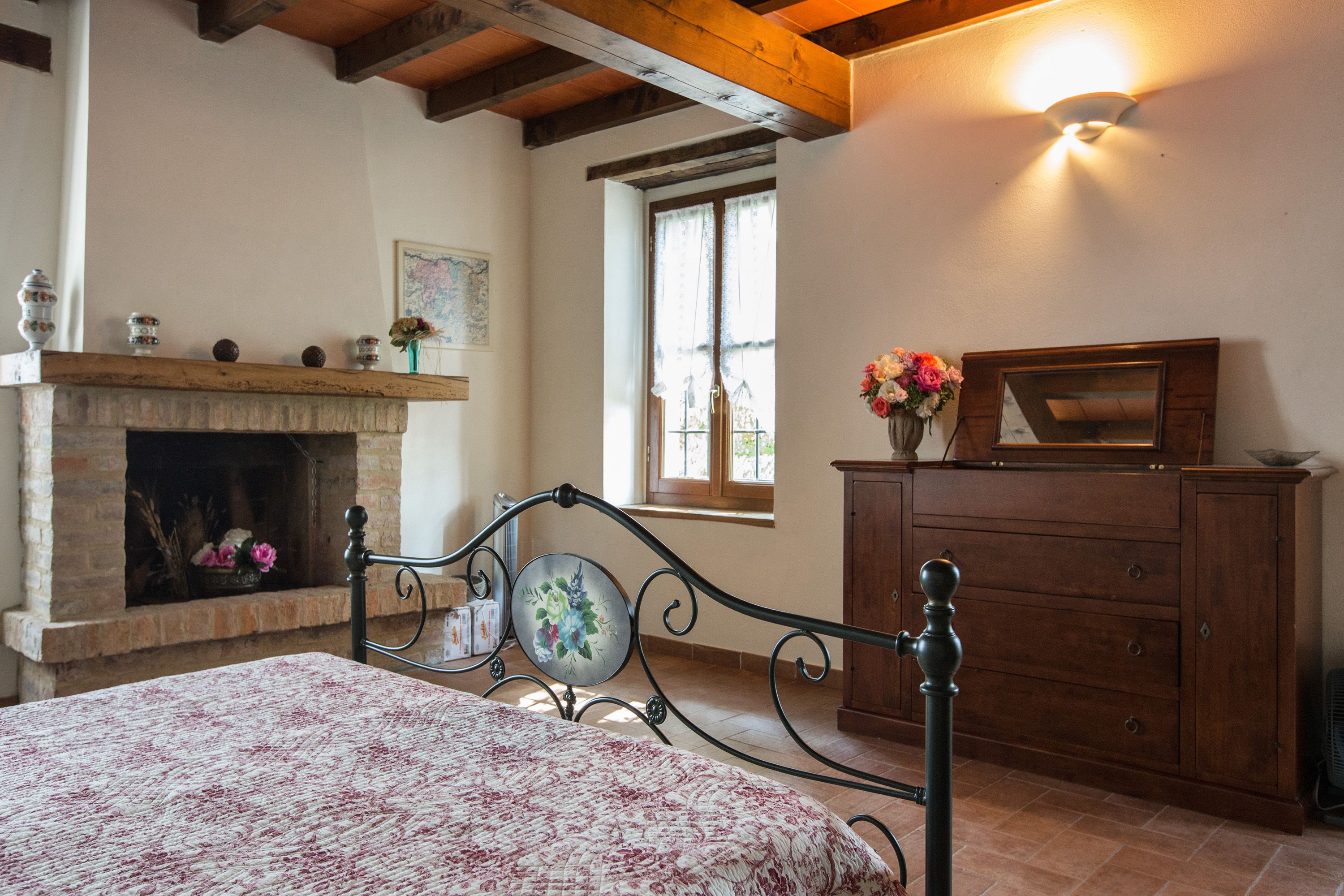 A bedroom with a bed, a fireplace, a dresser, and a window.
