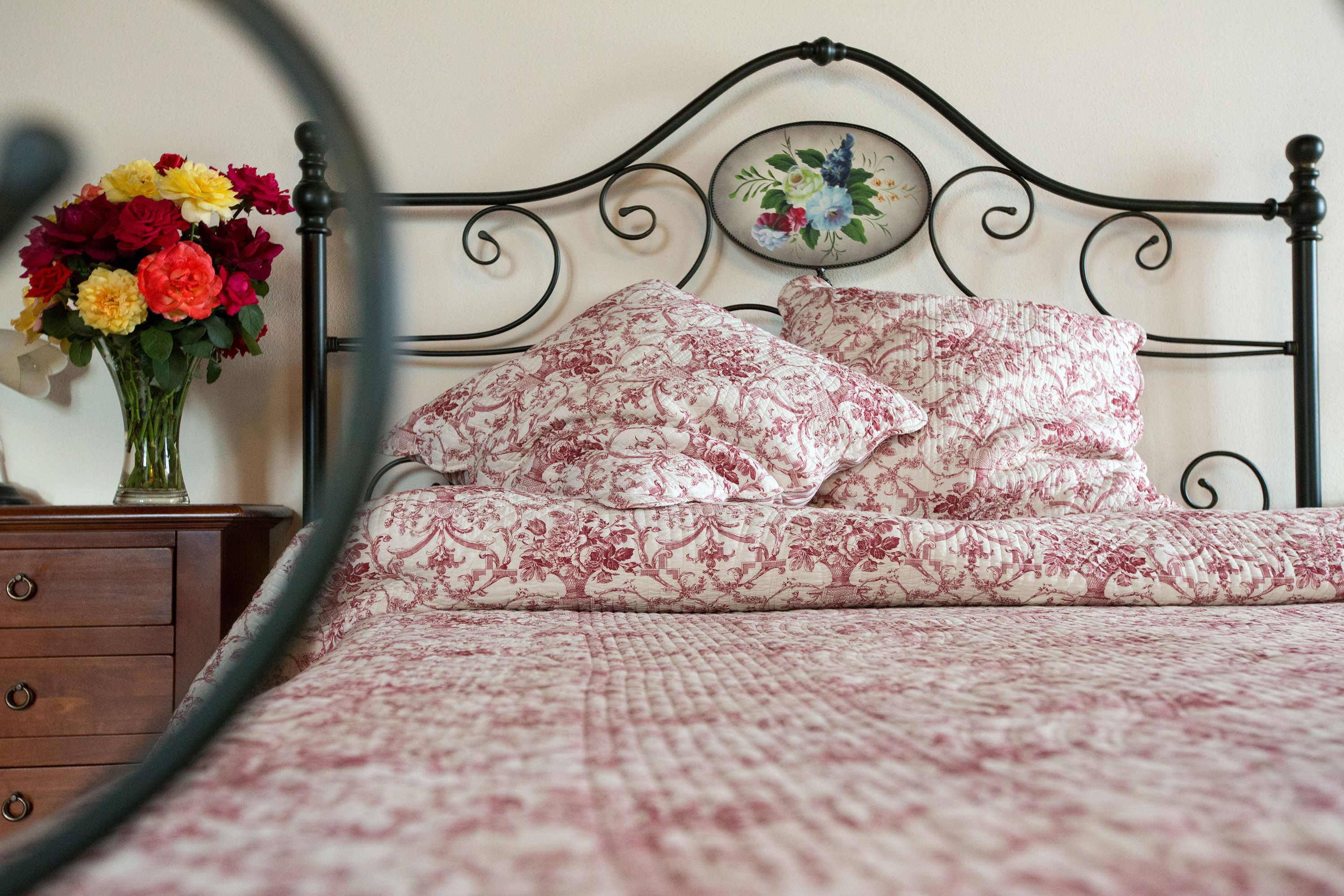 A bed with floral bedding, a nightstand with a vase of flowers, and a wall-mounted picture.