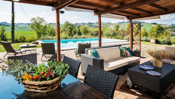 Ein überdachter Außenbereich mit Korbmöbeln, einem Pool und Blick ins Grüne.