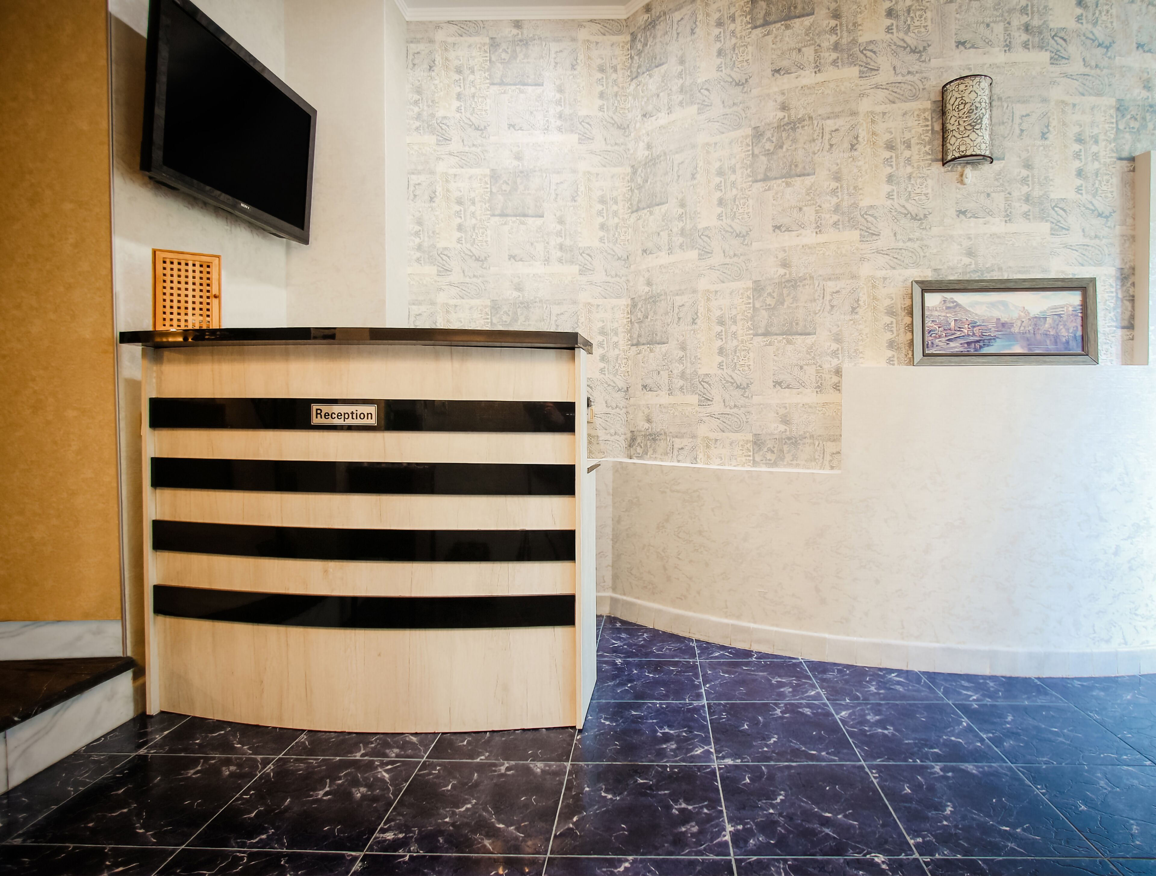 Ein Empfangsschalter mit einem Schild, einem Flachbildfernseher, strukturierten Tapeten und einem gerahmten Bild an der Wand.