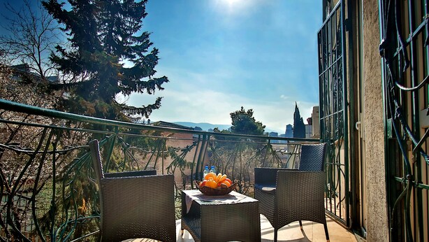 A balcony with two wicker chairs, a small table, and a bowl of oranges and bottles. - Hotel Toma's House (Tbilisi)