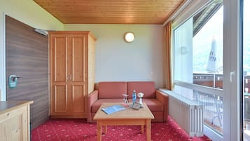 Una habitación acogedora con techo de madera, un sofá rojo con estampado, una mesa de madera con un libro y un jarrón, y una ventana con vistas a un edificio.