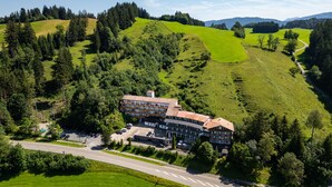 An aerial view of a hotel with multiple floors, surrounded by lush green hills and trees. - Rothenfels Panorama Hotel (Immenstadt im Allgaeu)