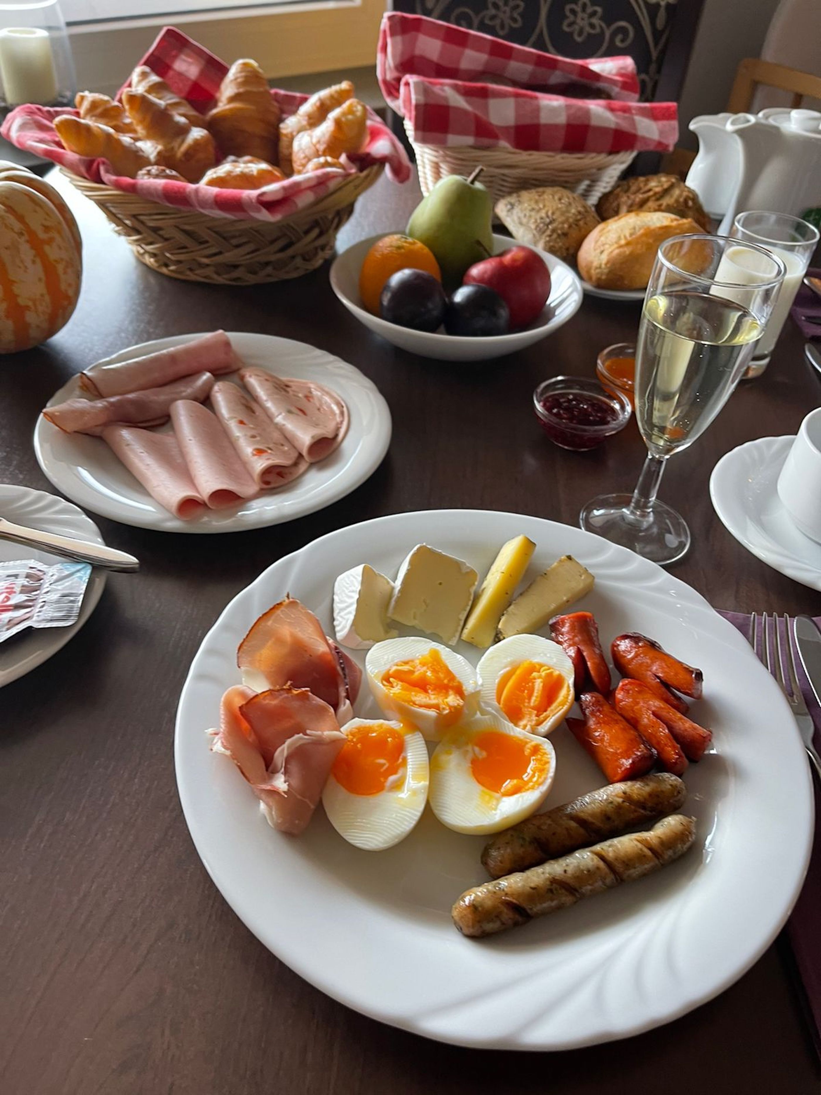 Un desayuno con varios alimentos, como jamón, huevos, salchichas, queso y productos de pastelería.