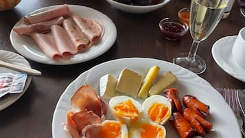 Un desayuno con varios alimentos, como jamón, huevos, salchichas, queso y productos de pastelería.