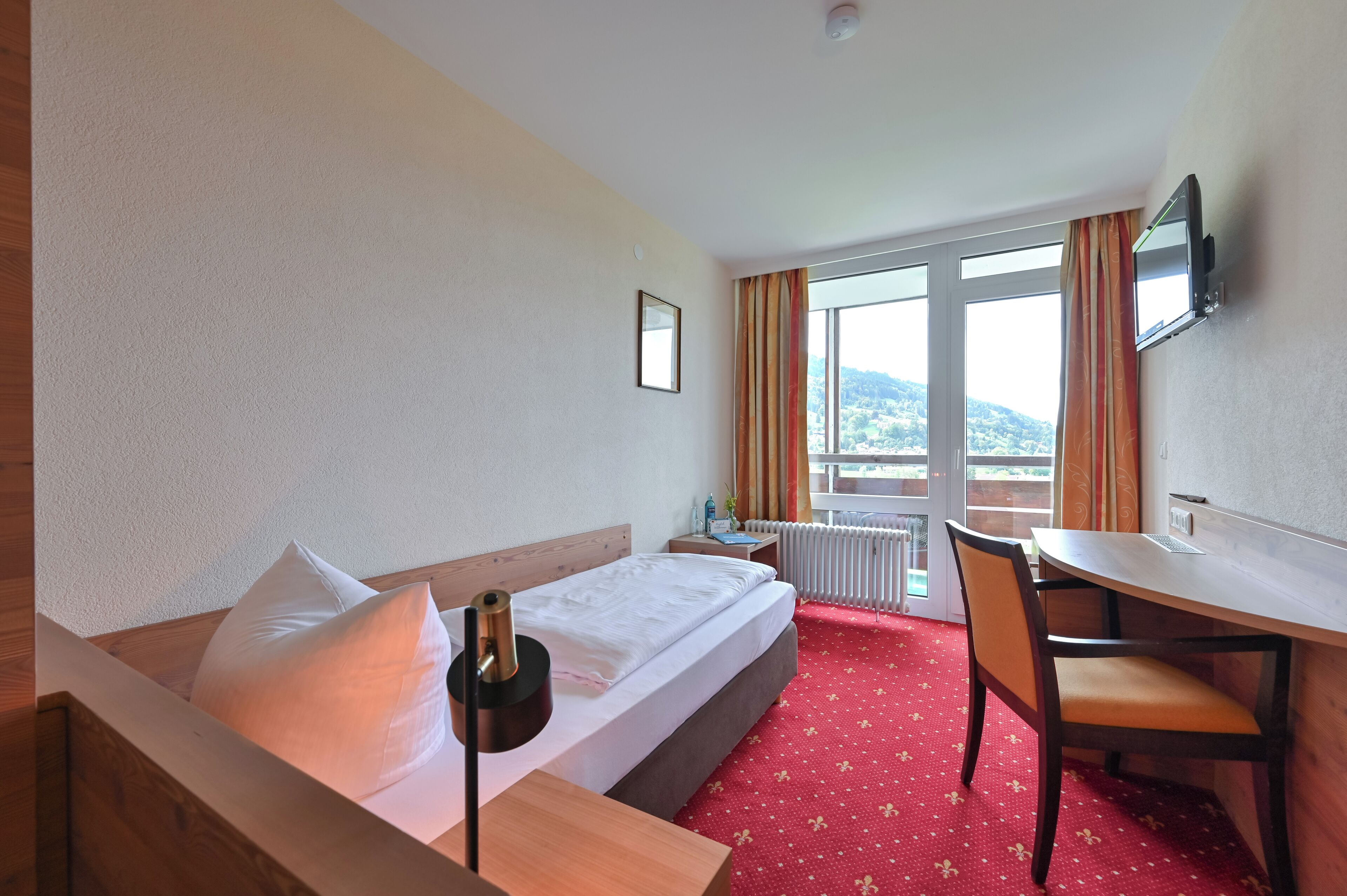 A hotel room with a bed, a desk, a chair, a television, and a window with curtains.