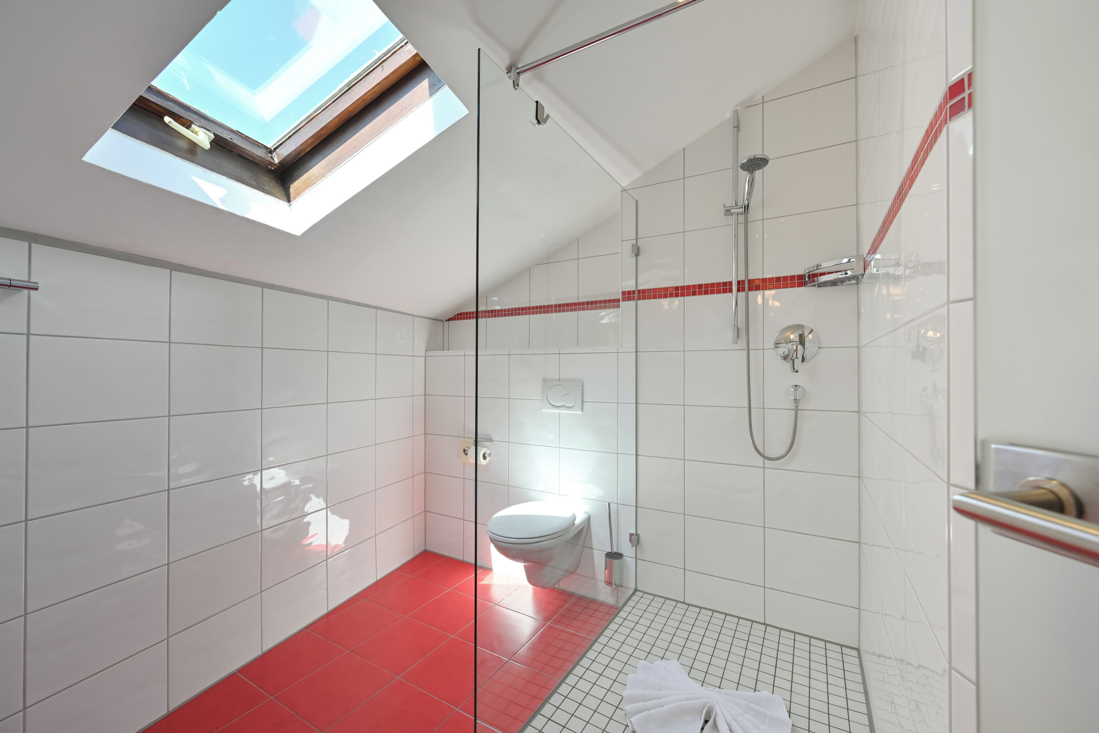 A modern bathroom with a skylight, a glass shower enclosure, and a red-tiled floor.