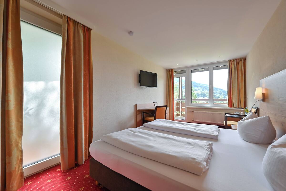 A hotel room with a bed, a desk, a chair, a television, and a window with curtains.