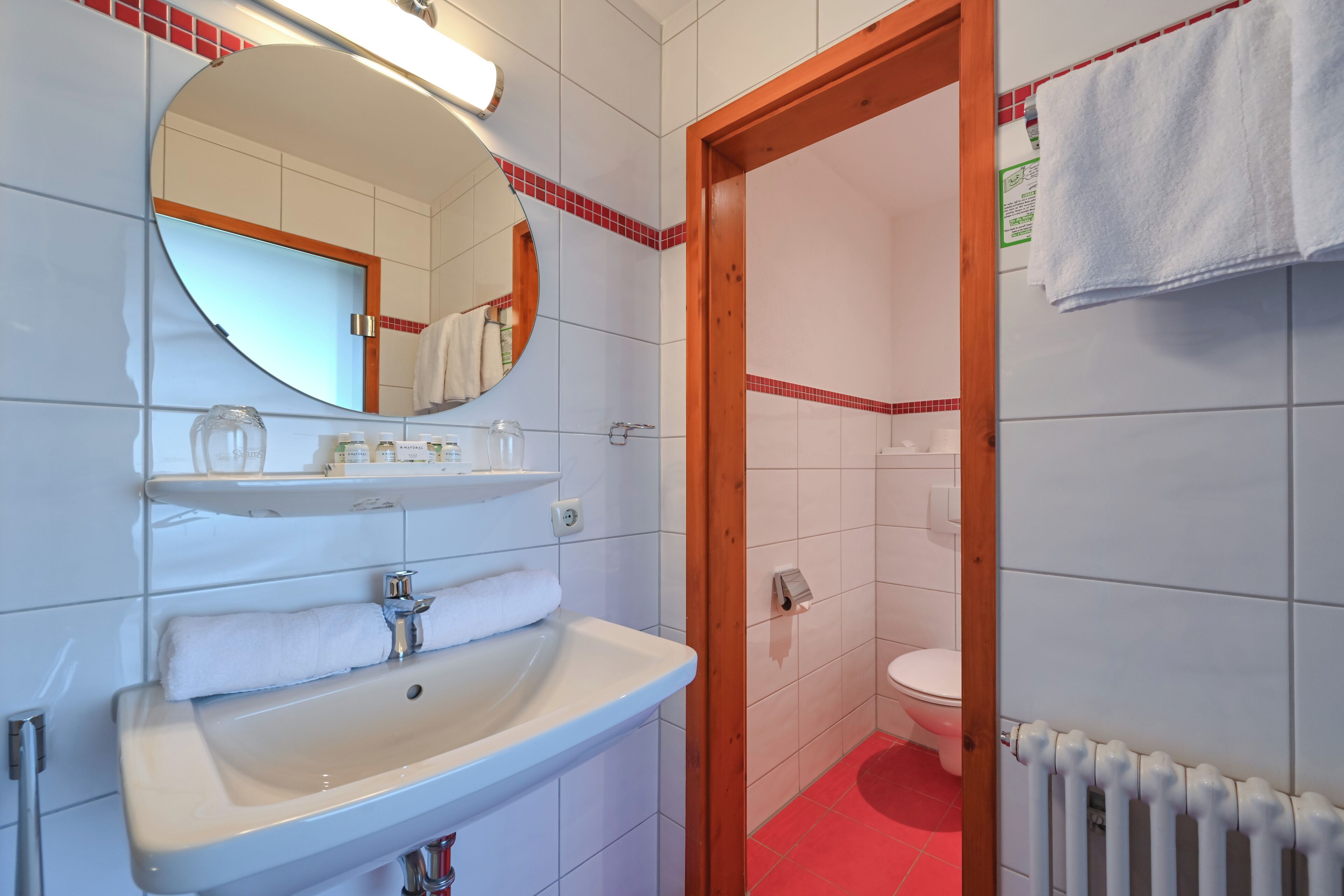 Un baño con lavamanos blanco, espejo y suelo de baldosas rojas.