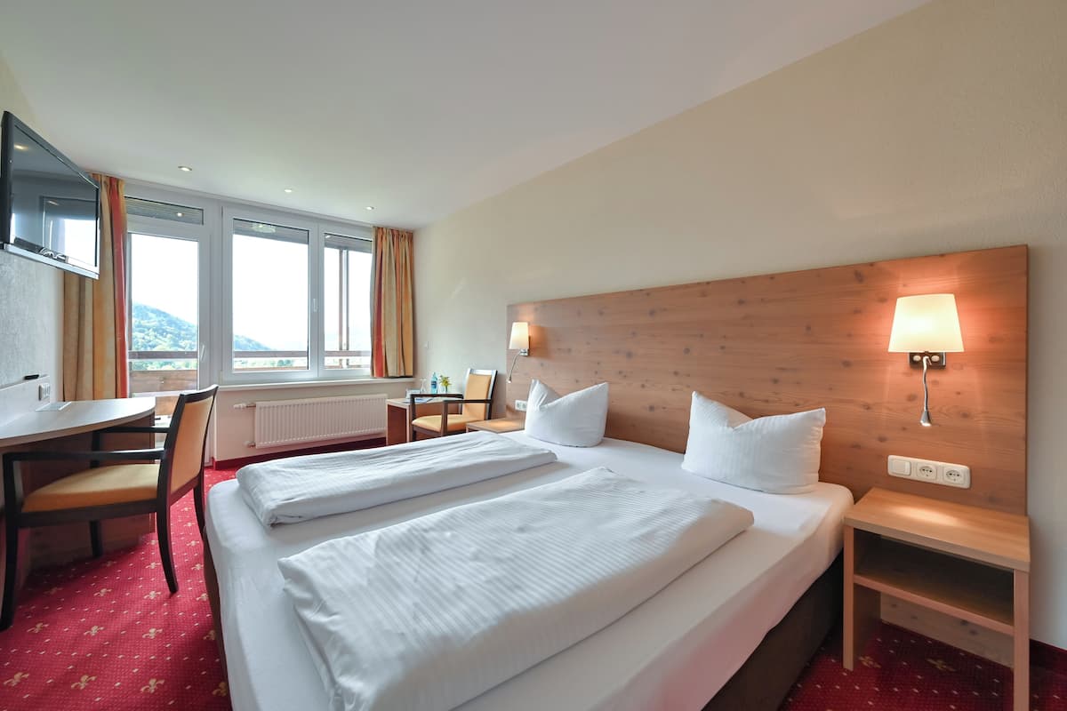 A hotel room with two beds, a desk, a chair, a TV, and a window with curtains.