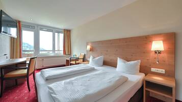 A hotel room with two beds, a desk, a chair, a TV, and a window with curtains.
