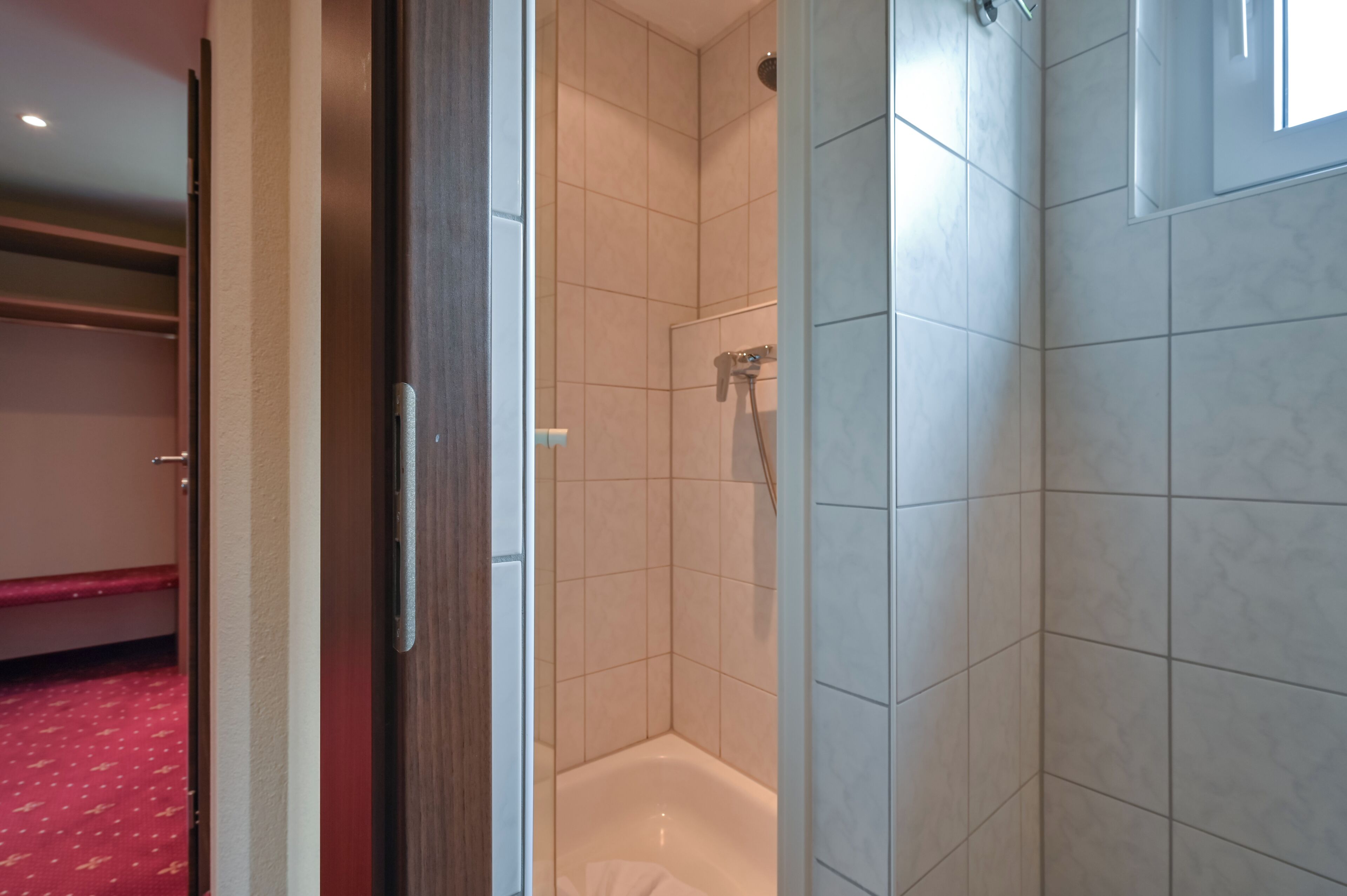 A hotel room with a shower, a bed with a red patterned bedspread, and a wooden door.
