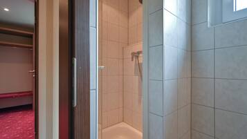 A hotel room with a shower, a bed with a red patterned bedspread, and a wooden door.