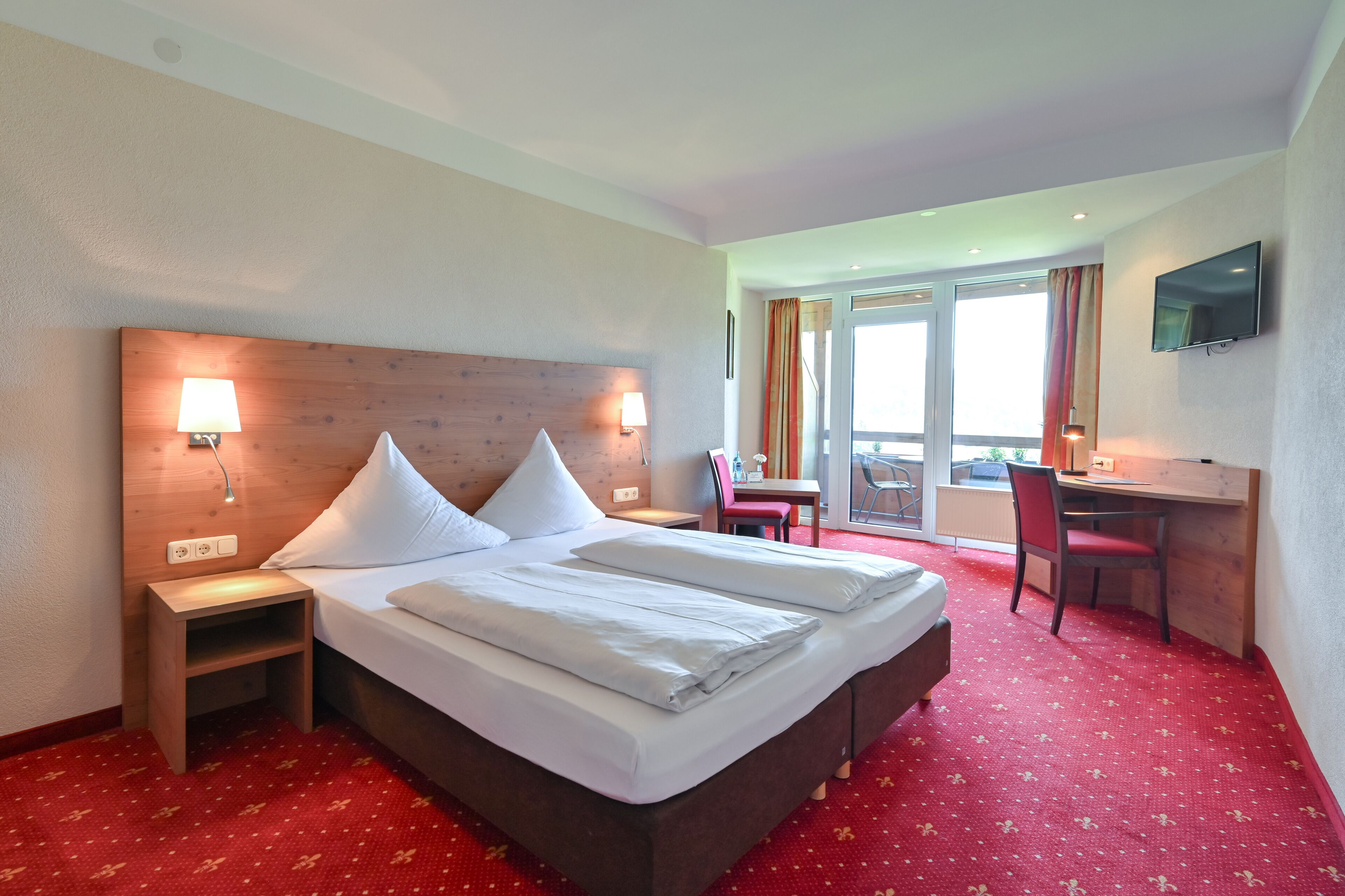 Habitación de hotel con una cama grande, un escritorio, una silla y un televisor en la pared.