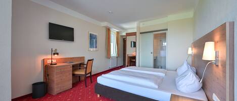 A hotel room with a bed, desk, chair, and a TV mounted on the wall.
