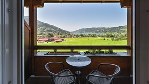 A balcony with a view of a green valley and mountains. There are two wicker chairs and a small round table. - Rothenfels Panorama Hotel (Immenstadt im Allgaeu)