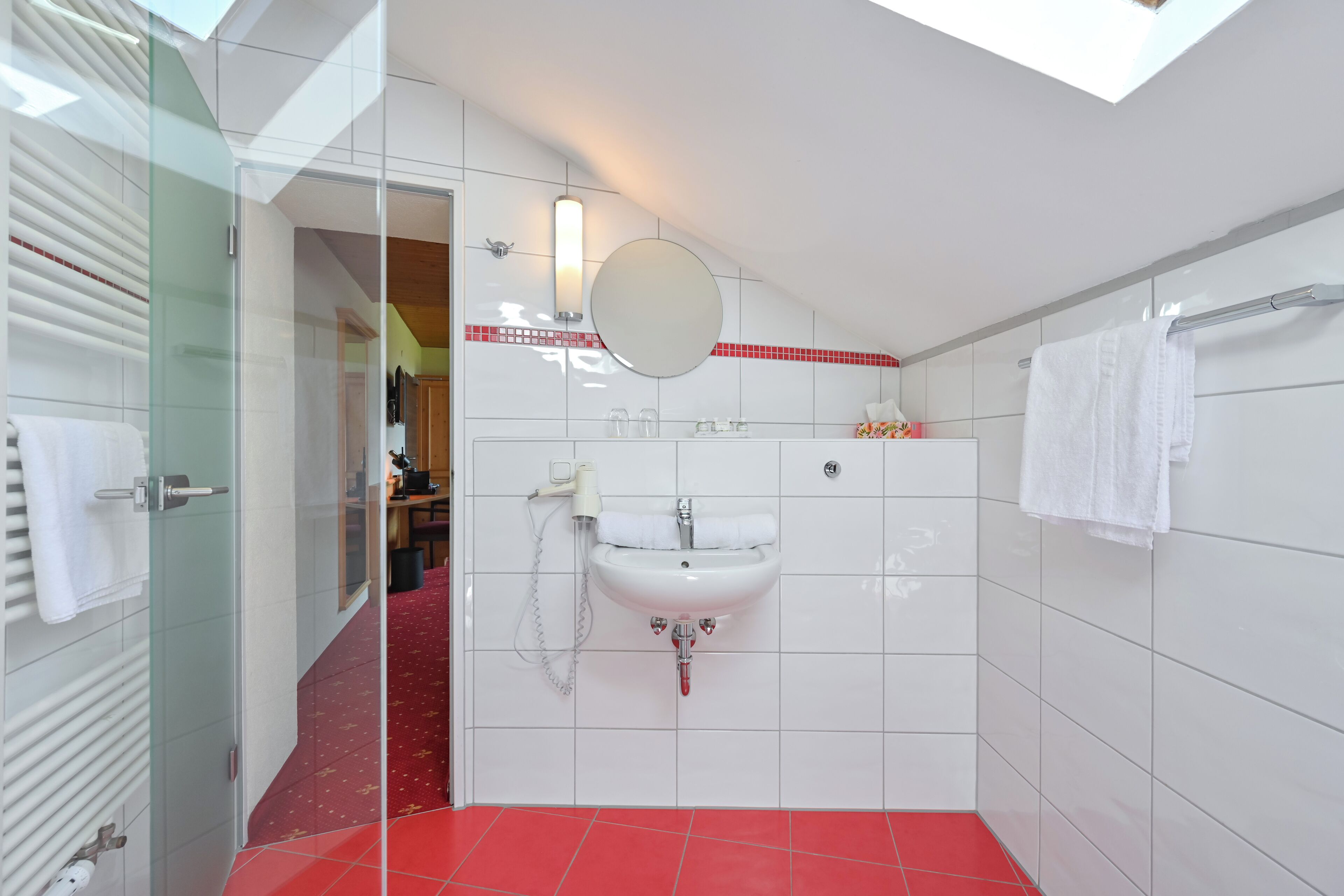 Une salle de bain moderne avec une douche à parois de verre, un lavabo blanc avec un miroir et un sol carrelé de carreaux rouges.