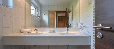 A modern bathroom with two sinks, a large mirror, and a wooden door.