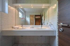 A modern bathroom with two sinks, a large mirror, and a wooden door. - Rothenfels Panorama Hotel (Immenstadt im Allgaeu)