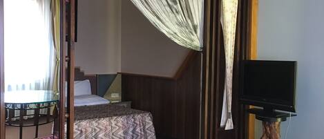 A hotel room with a bed, a glass table, a television, and a window with curtains.
