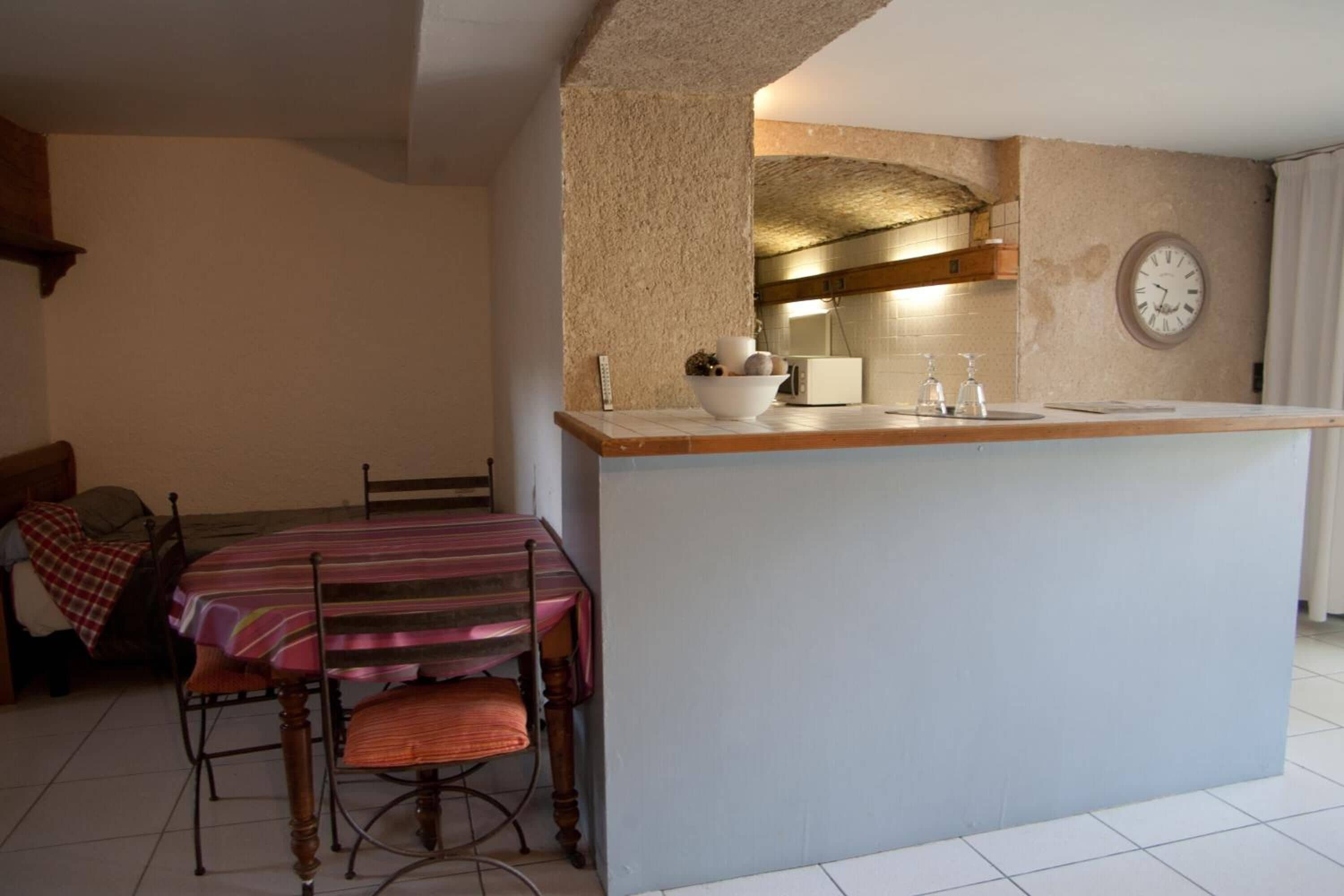 Une cuisine avec un îlot central, une table à manger avec des chaises et une horloge au mur.