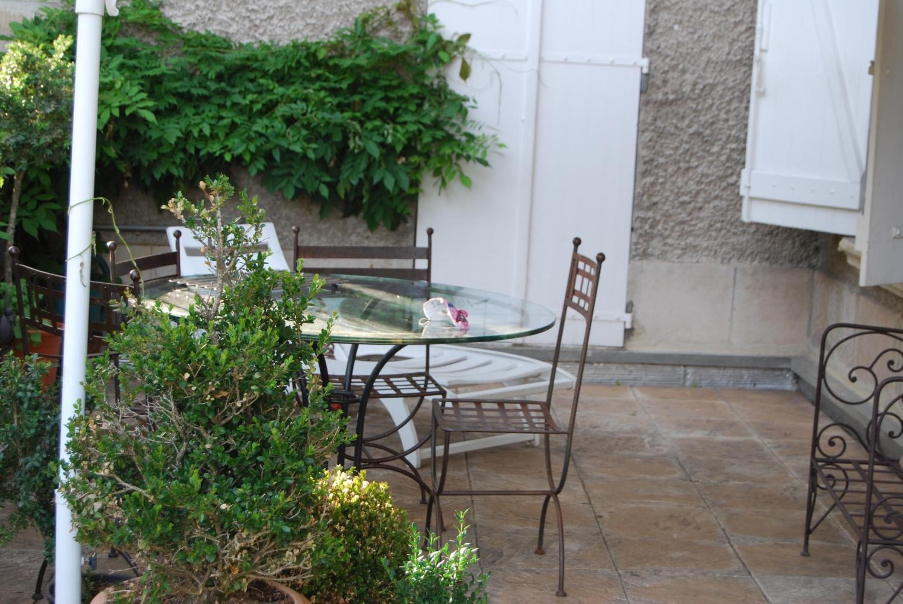 A glass-top table with metal chairs, surrounded by potted plants and a stone-tiled patio.