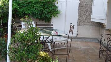 A glass-top table with metal chairs, surrounded by potted plants and a stone-tiled patio.