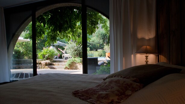 Un dormitorio con un ventanal grande, una cama con un edredón estampado floral y una lámpara.