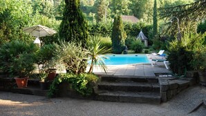 Un área de piscina con escalones que conducen al agua, rodeada de plantas en macetas y un pequeño pabellón.