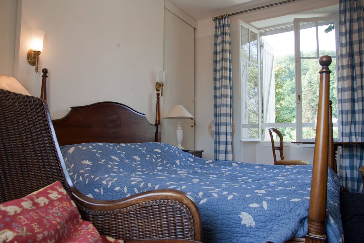 Une chambre à coucher avec un lit, une chaise, une lampe et une fenêtre avec des rideaux.