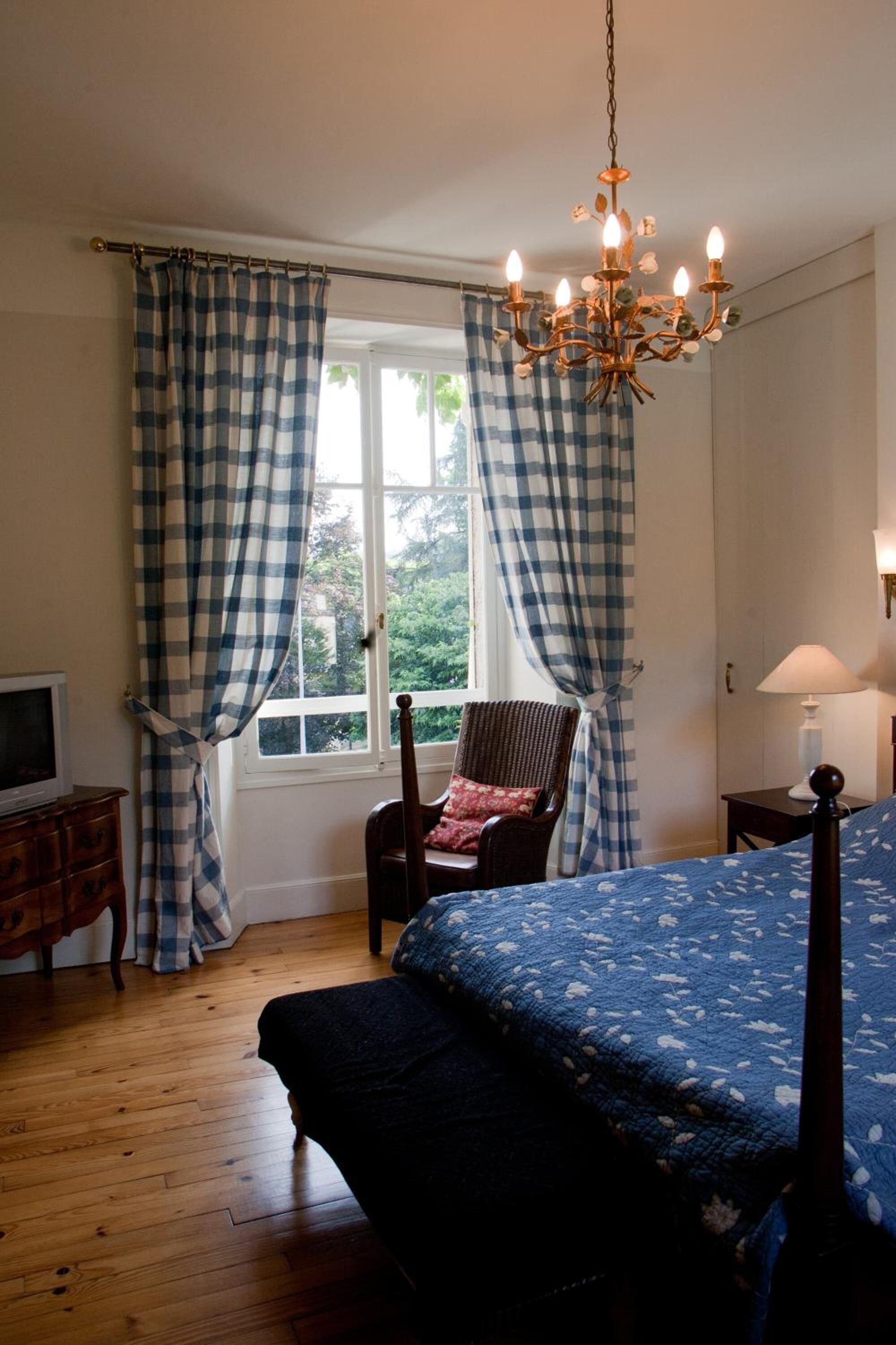 A bedroom with a bed, a chair, a television, a lamp, and a window with curtains.