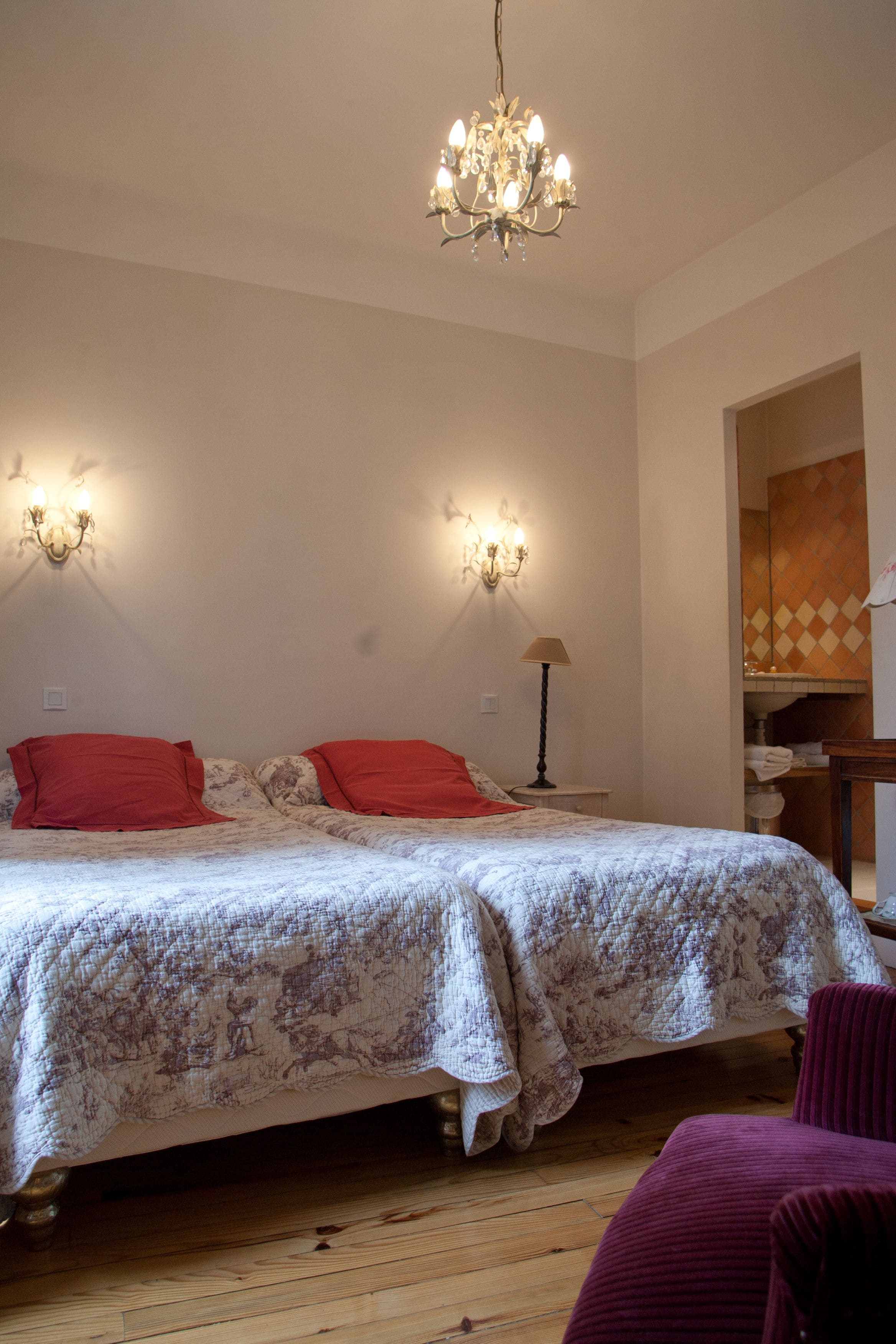 Quarto com uma cama grande, duas almofadas vermelhas, um candelabro e uma mesa de cabeceira com abajur.