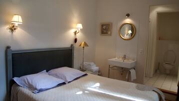 Une chambre d’hôtel comprenant un lit, une lampe de chevet, un miroir fixé au mur et une salle de bain avec un lavabo et des toilettes.