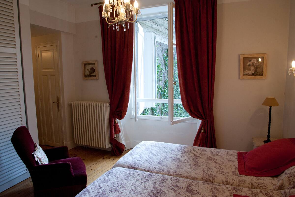 Une chambre à coucher avec un lit, une chaise, une fenêtre avec des rideaux, un radiateur et une lampe.