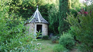 Un edificio de piedra con techo cónico en un jardín exuberante.