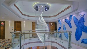 Un moderno vestíbulo de hotel con una escalera espiral central, barandilla de vidrio y un techo con lámpara decorativa.