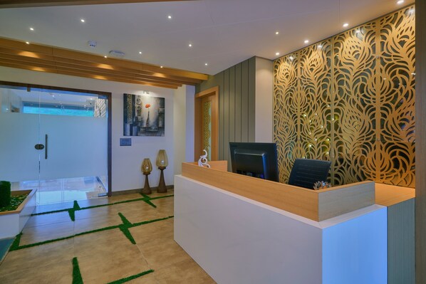 Zona de recepción con mostrador de madera, pared con diseño y puerta de cristal que da a un balcón.